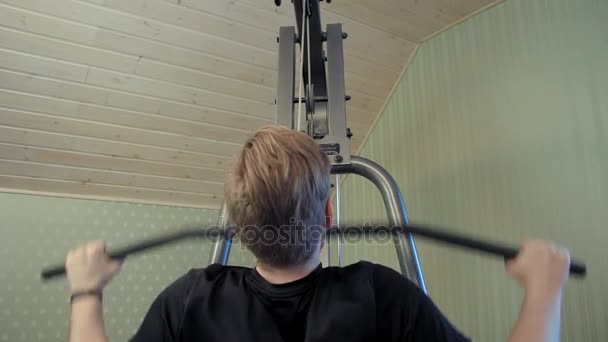 Young man works out on his home gym equipment to exercise his shouloder muscles - Metraje, vídeo