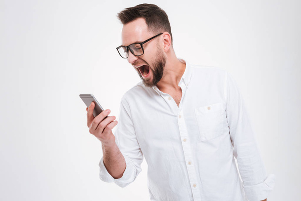 Screaming angry young bearded man holding phone - Zdjęcie, obraz