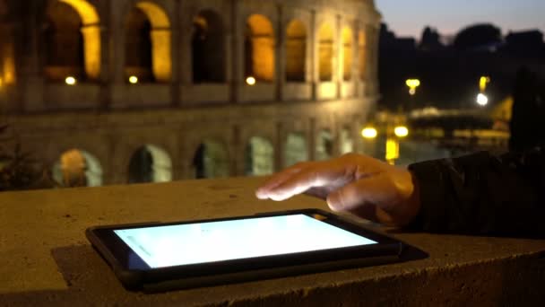 man hand using tablet leaning against a wall with the coliseum background - Filmati, video