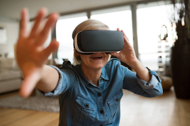 Senior woman wearing virtual reality goggles at home - Photo, Image