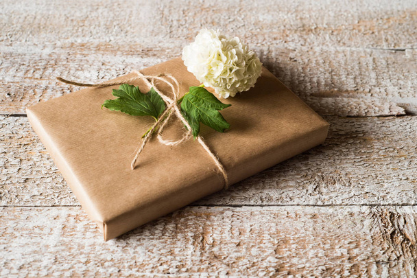 Present wrapped in brown paper, lilac flower laid on it. - Foto, afbeelding