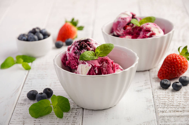 Ice cream with blueberries and strawberries in white bowl on white wooden background - Photo, Image