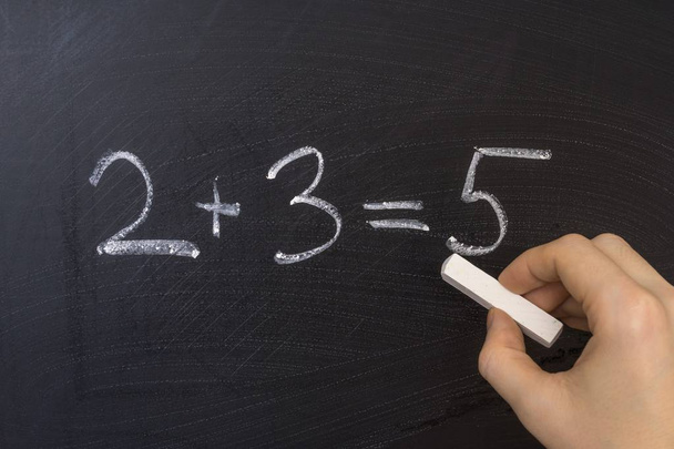 Teacher is writing simple math equation on blackboard with chalk. Education in elementary school concept. - Photo, Image