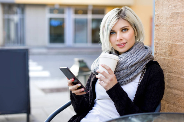 Nő mozgatható telefon, és a járdán Cafe kávéscsésze - Fotó, kép