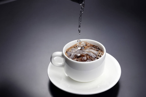 gekookt water wordt gegoten in een witte kop met zwarte koffie - Foto, afbeelding