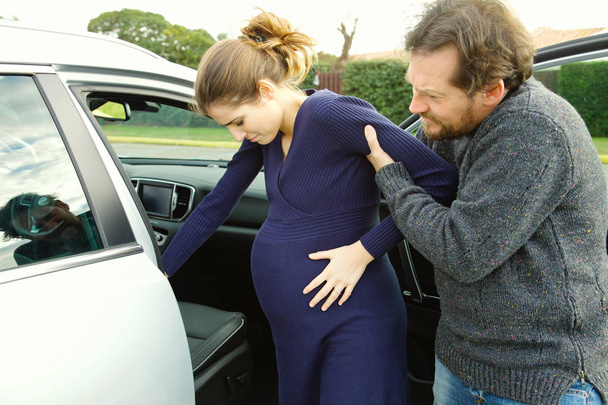 Pregnant woman feeling pain helped to get into car by boyfriend - Foto, immagini