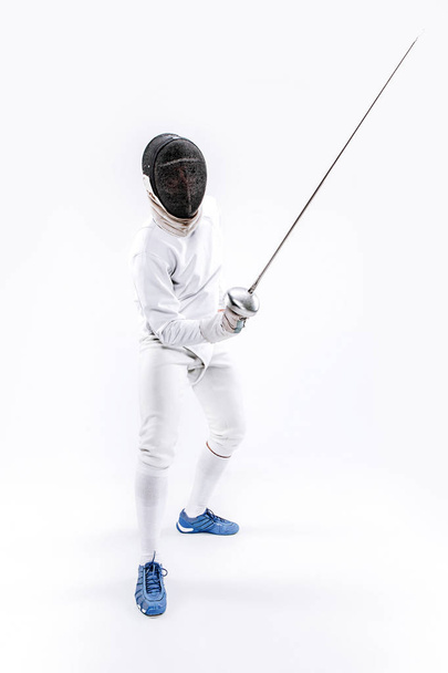 Man wearing fencing suit practicing with sword against gray - Фото, изображение