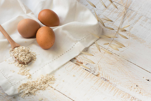 frische Bio-Eier, trockene Haferflocken auf Holzlöffel über weißes Leinentuch verstreut, Holzhintergrund, gesunde Zutaten, achtsames Essen, Schönheit, Hautpflege - Foto, Bild