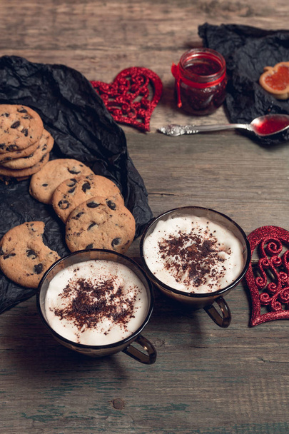 Romantic breakfast. Two Cups of coffee, cappuccino with chocolate cookies and biscuits  near red hearts on wooden table background. Valentine day. Love. Top view.  - Фото, зображення