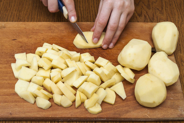 Το χέρι της γυναίκας με ένα μαχαίρι κοπής σε φέτες πατάτες σε ξύλινα Μπόα - Φωτογραφία, εικόνα