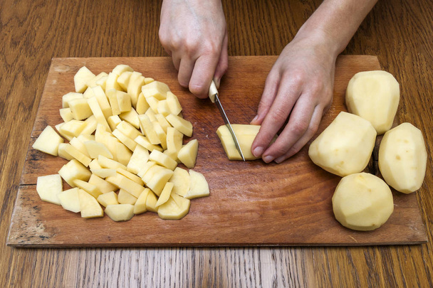 Woman's hand with a knife cutting slicing potatoes on wooden boa - Photo, image