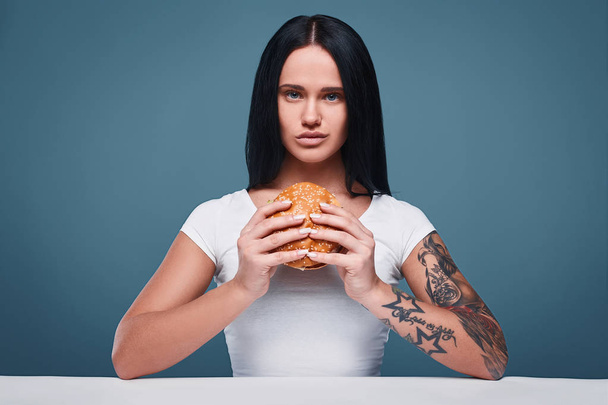 Красива чарівна дівчина татуювання тримає гамбургер
 - Фото, зображення