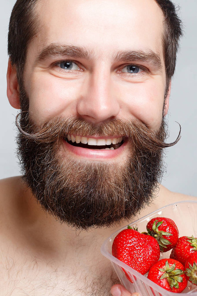 close-up portrait young man holding a strawberry and smiling - Photo, Image
