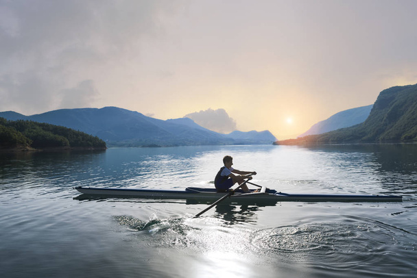 Young single scull rowing on lake - Fotó, kép