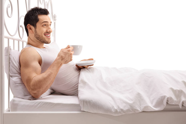 man lying in bed and holding a cup - Фото, изображение