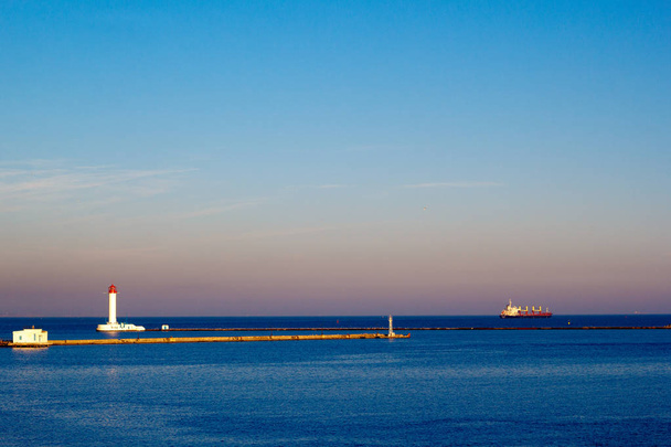 Lighthouse and Cargo ship leaving a harbor in the evening - Photo, Image