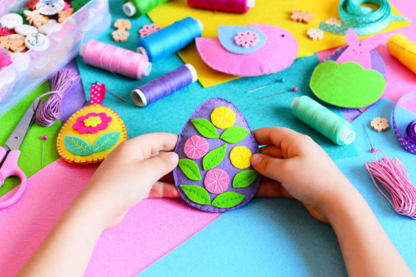 Çocuk Paskalya yortusu yumurta dekor elinde tutar. Küçük çocuk onun Paskalya el sanatları gösterir. Renkli Paskalya yumurta, tavşan ve kuş dekorasyonlar, dikiş malzemeleri ve araçları bir tabloda hissettim. Çocuklar için basit tatil DIY - Fotoğraf, Görsel