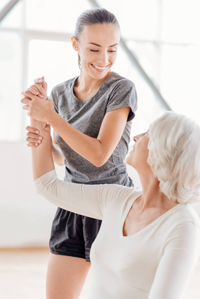 Joyful fitness coach looking at the elderly woman - Foto, immagini