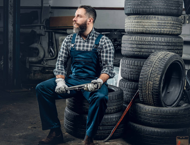 Mechaniker sitzt auf einem alten Reifen - Foto, Bild