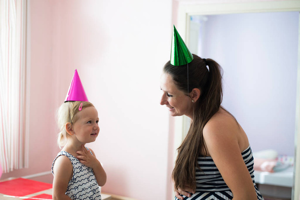 Beautiful mother with her cute daughter wearing party hats - Foto, Imagen