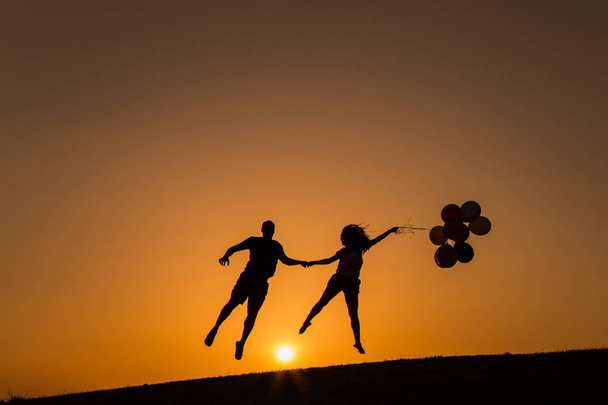 silueta de una pareja jugando con globos al atardecer
 - Foto, imagen