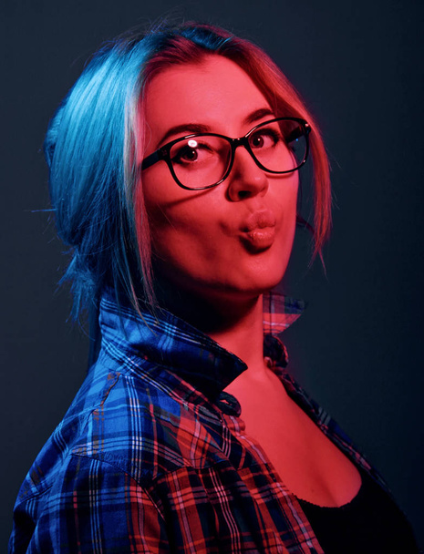 Blonde girl in a checkered shirt and eyeglasses. Kising lips.Red and blue lights.Portrait. - 写真・画像