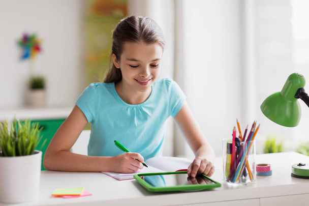 girl with tablet pc writing to notebook at home - Photo, Image