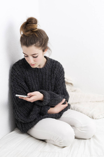 Jonge vrouw kijken naar de mobiele telefoon op een witte achtergrond.  - Foto, afbeelding