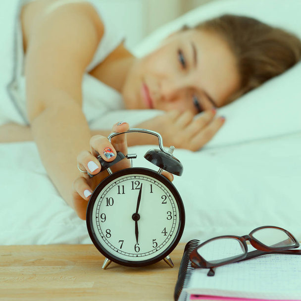 A young woman putting her alarm clock off in the morning - Фото, изображение