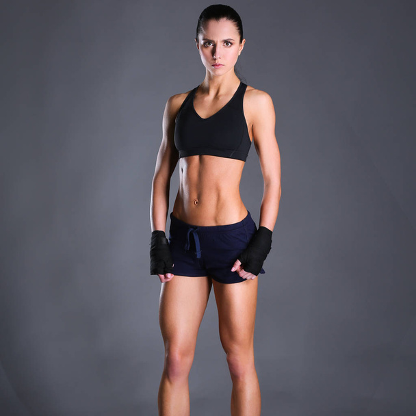 Muscular young woman posing in sportswear against black background - Φωτογραφία, εικόνα