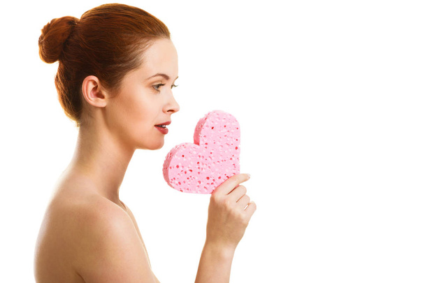 Woman naked shoulders holds pink heart shaped sponge. - Foto, imagen