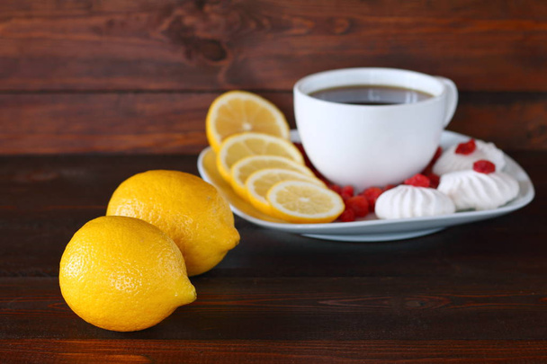 Sitruuna, musta tee ja makeiset ovat tummalla puupohjalla
. - Valokuva, kuva