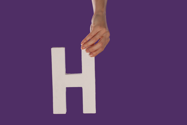 Mano femenina sosteniendo la letra H desde arriba
 - Foto, Imagen