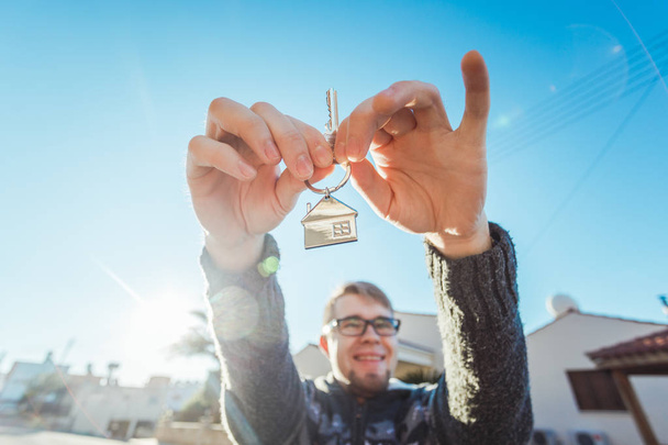 Happy funny man holds house keys on house shaped keychain in front of a new home - Photo, Image