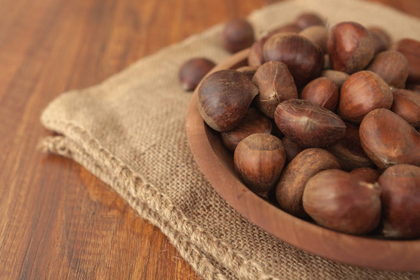 Chestnuts in a wooden bowl on a sackcloth. - Fotografie, Obrázek