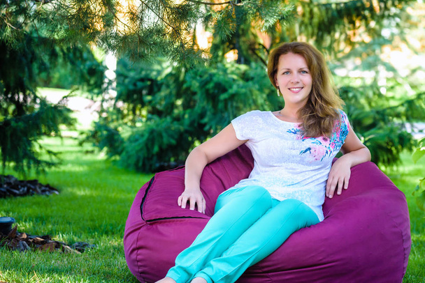 Girl relaxing in a bean bag chair on the green grass - Photo, Image