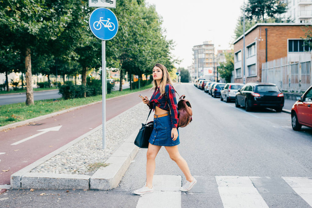 woman crossing pedestrian rossing using smartphone - Fotó, kép