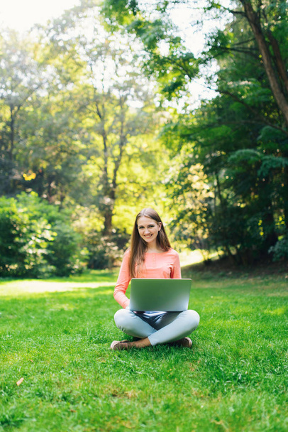 Student girl working with a laptop in a green park - Фото, изображение