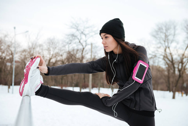 Woman with armband stretching legs before running outdoors - Photo, image