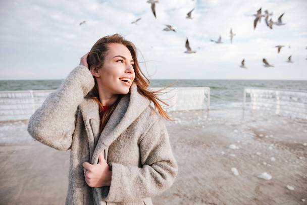 Cheerful cute young woman walking on pier in winter - Фото, изображение