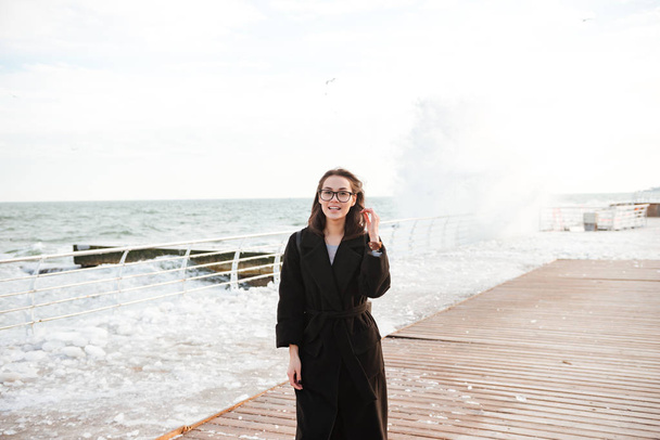 Happy young woman wearing glasses standing on pier in winter - Zdjęcie, obraz