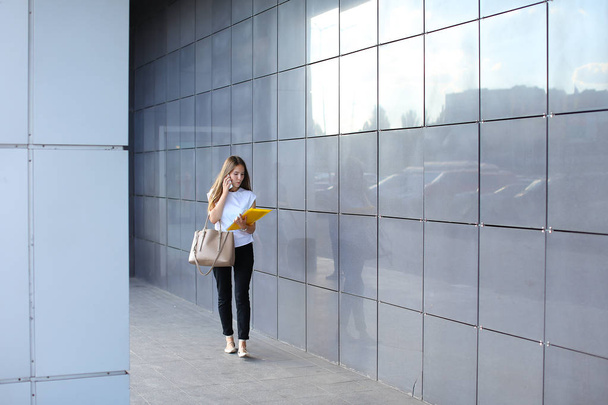 Νεαρή γυναίκα περπατά και μιλά στο τηλέφωνο, κατέχει έγγραφα σε - Φωτογραφία, εικόνα