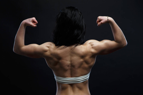 Атлетичная молодая женщина показывает мышцы спины и рук
 - Фото, изображение