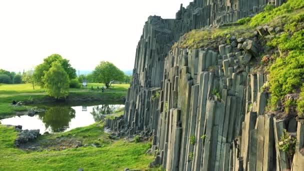 A columnar basalt rock overgrown with bushes near a lake - Footage, Video