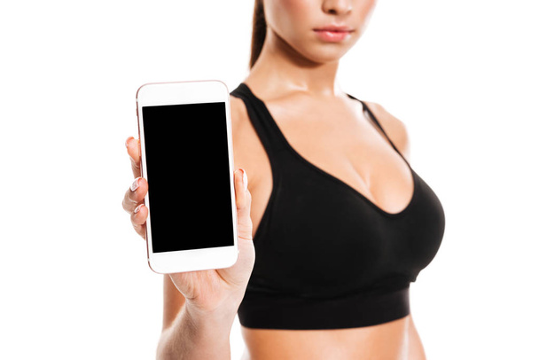 Young pretty fitness woman showing blank screen mobile phone - Fotó, kép