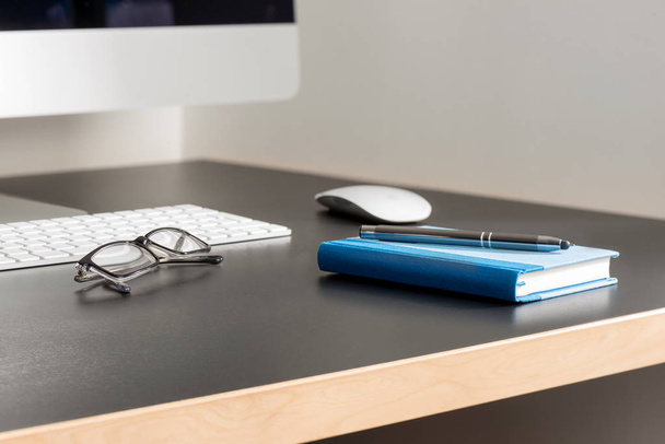 Γκρι γραφείο με υπολογιστή, γυαλιά, στυλό και σημειωματάριο  - Φωτογραφία, εικόνα