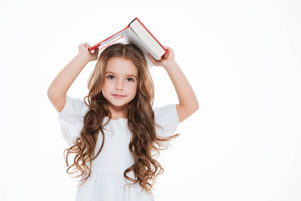 Pretty little girl standing and holding book above her head - Фото, зображення