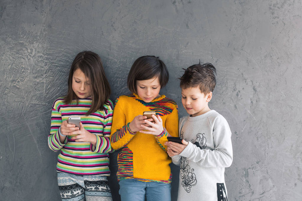 Grupa młodych dziewcząt i chłopca gry w telefonie, uśmiecha się i śmieje się. Dzieci uczą się nowych technologii - Zdjęcie, obraz