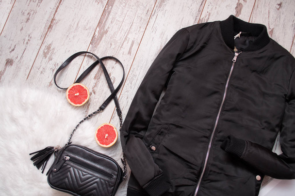 Чорна куртка і сумка на білому хутрі, грейпфруті, дерев'яному фоні. Концепція моди. Вид зверху
 - Фото, зображення