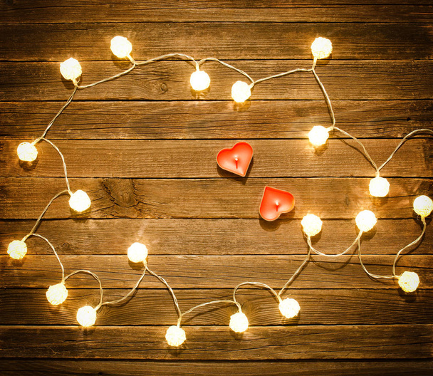 Two candles in the shape of heart among the glowing lanterns made of rattan on a wooden background. View from above, space for text - Zdjęcie, obraz